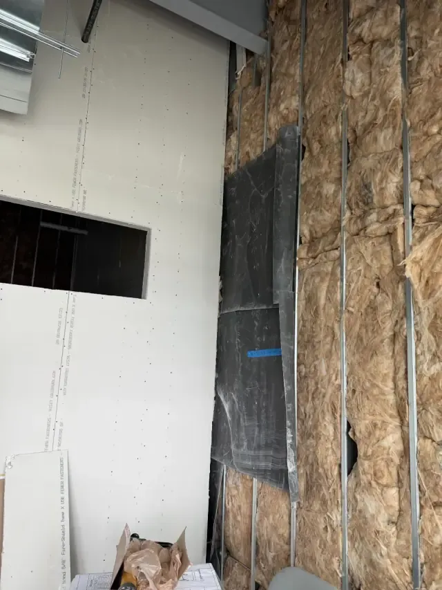Close detail of a studio wall mid-build with insulation, sound-control membrane, and drywall going up.
